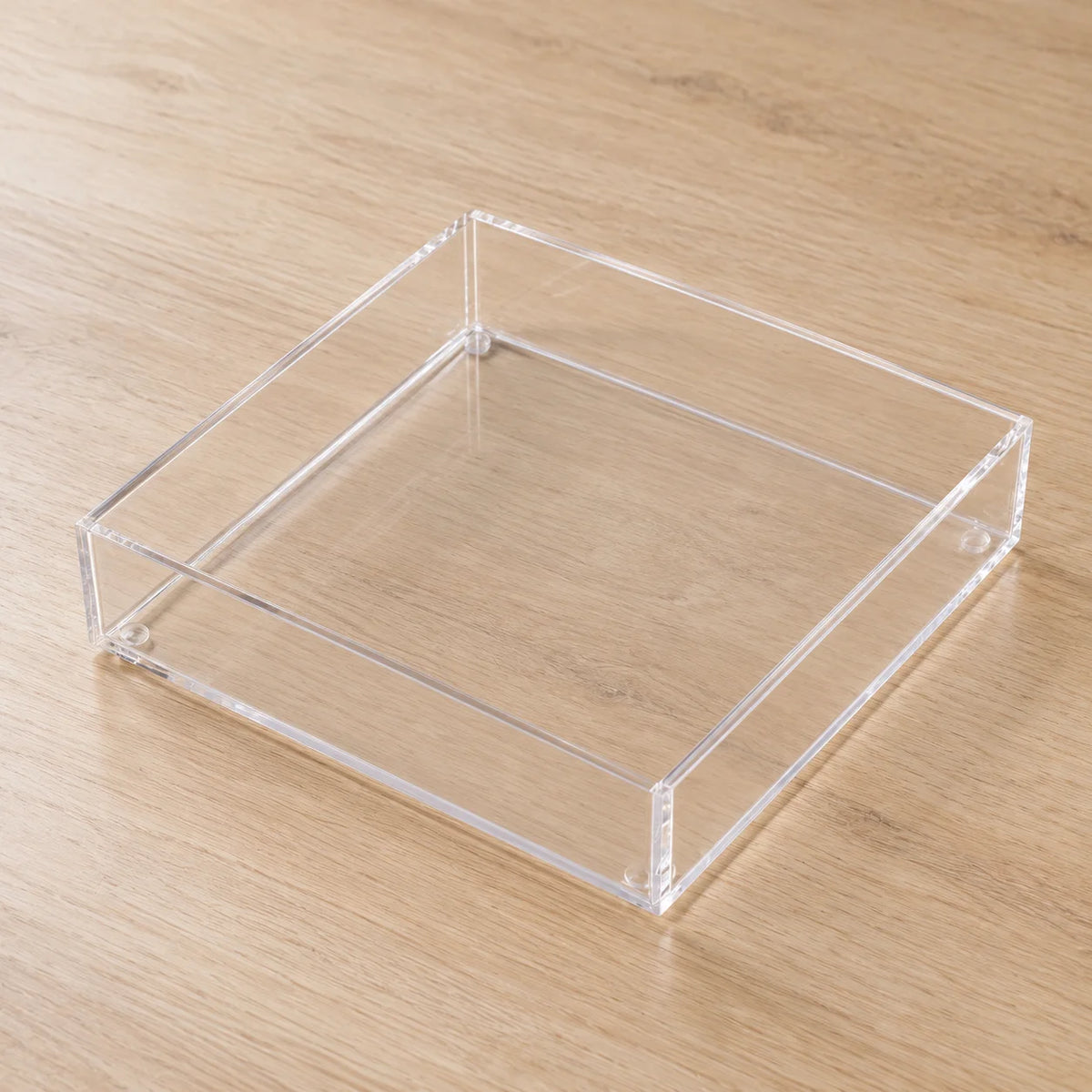 Caixa organizadora Velune em acrílico cristal, quadrada e vazia sobre mesa.