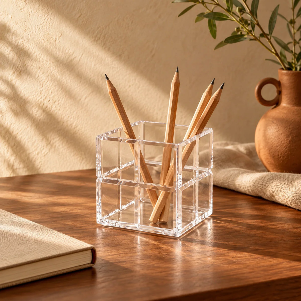 Cubo organizador Faceta em acrílico cristal, com lápis e pincéis sobre mesa.