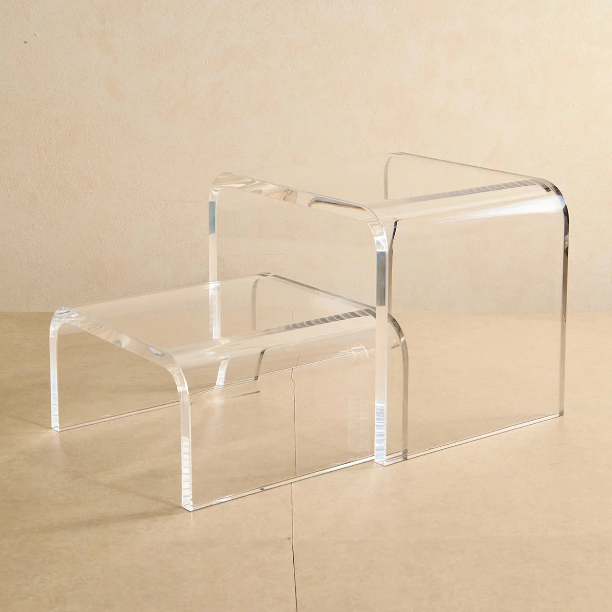Escada modular Altea em acrílico cristal, com dois degraus sobre fundo bege.