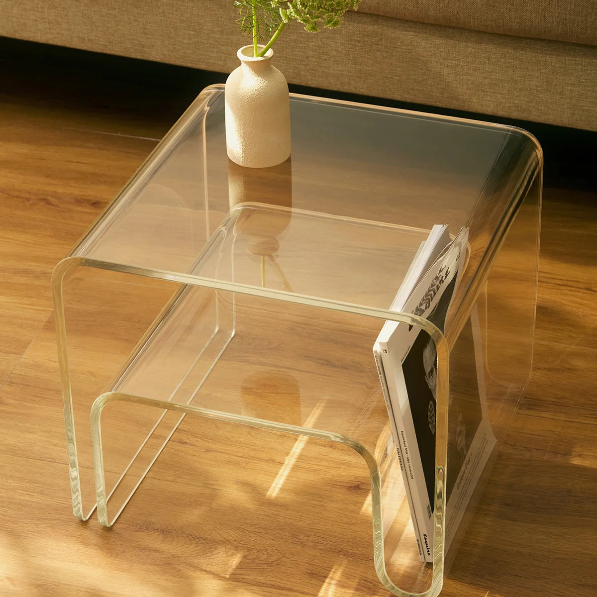 Mesa lateral Vértis em acrílico cristal, com vaso e livro em sala iluminada.