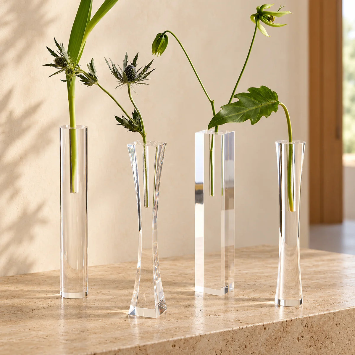 Vasos Lumielle em acrílico cristal, com quatro formatos e arranjos de folhagens.