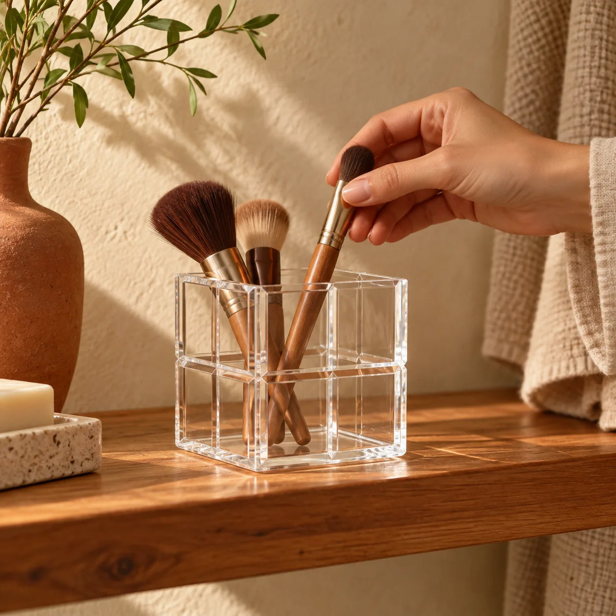 Cubo organizador Faceta em acrílico cristal, com mão retirando pincel de maquiagem.