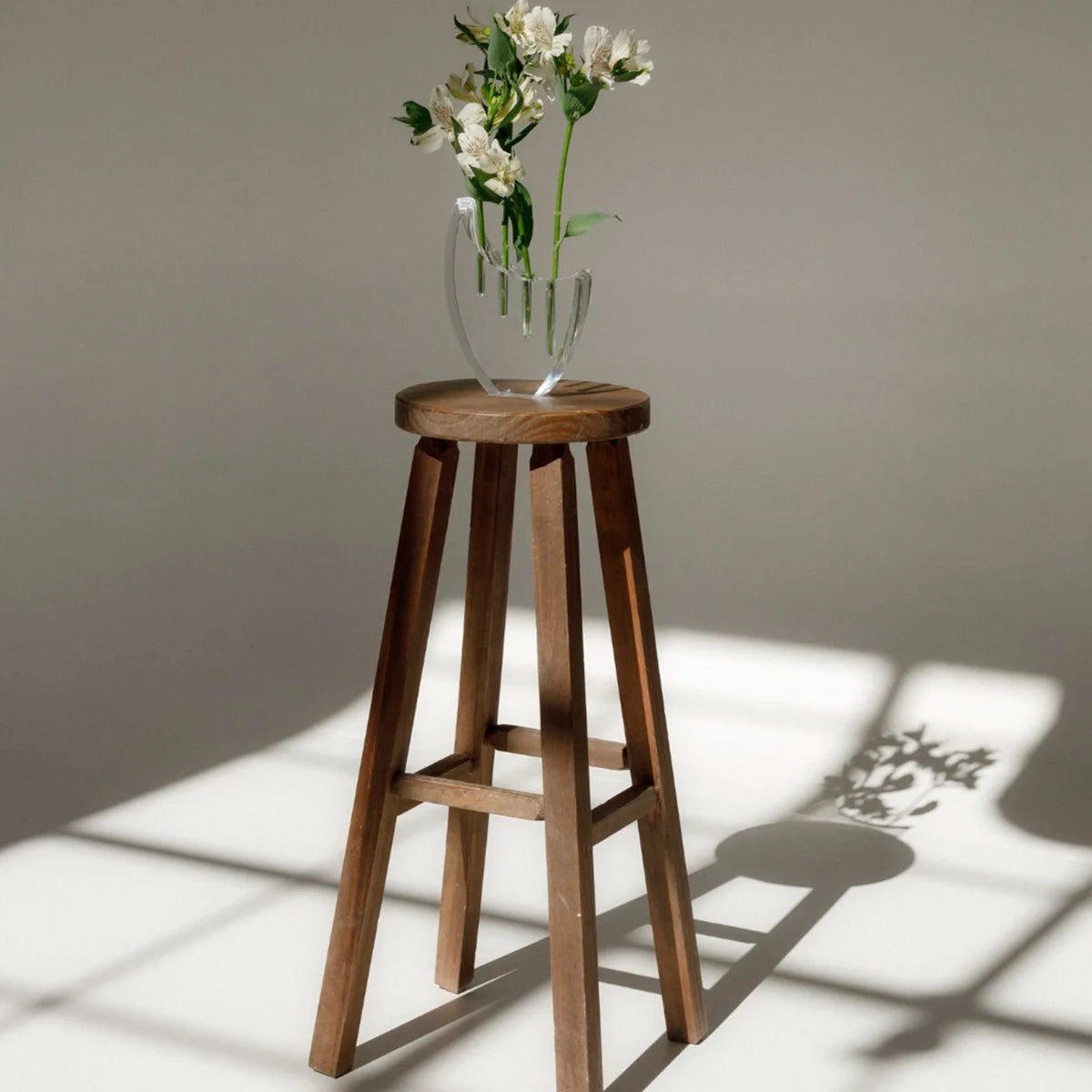 Vaso Selene em acrílico cristal, com flores sobre banco de madeira.