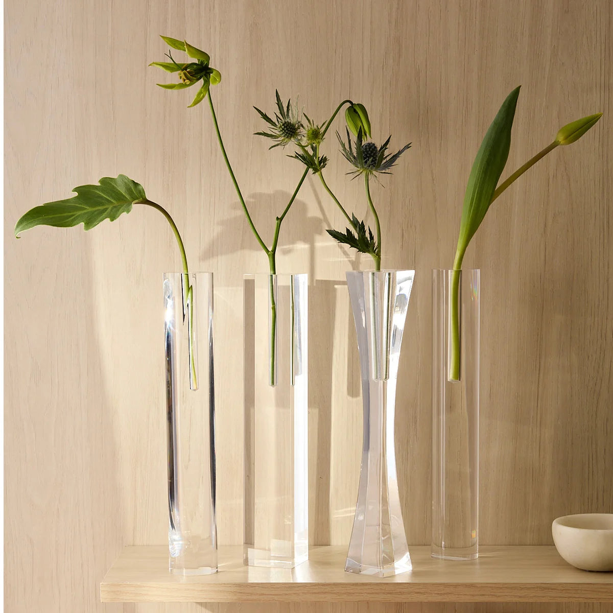 Vasos Lumielle em acrílico cristal, em detalhe do conjunto com folhagens.