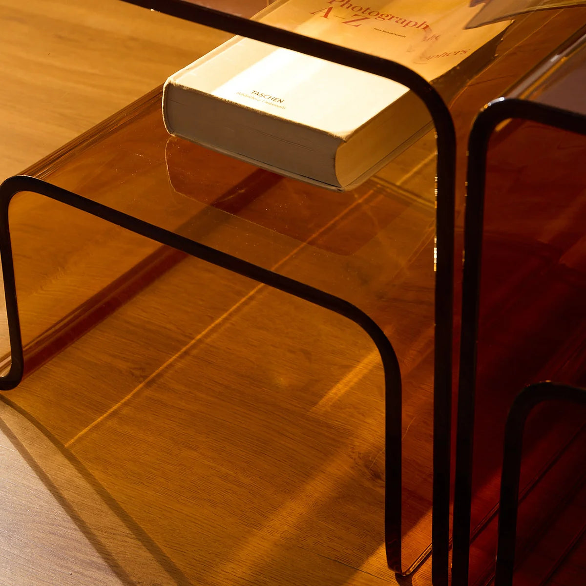 Mesa lateral Vértis em acrílico âmbar, em detalhe do tampo com livro.