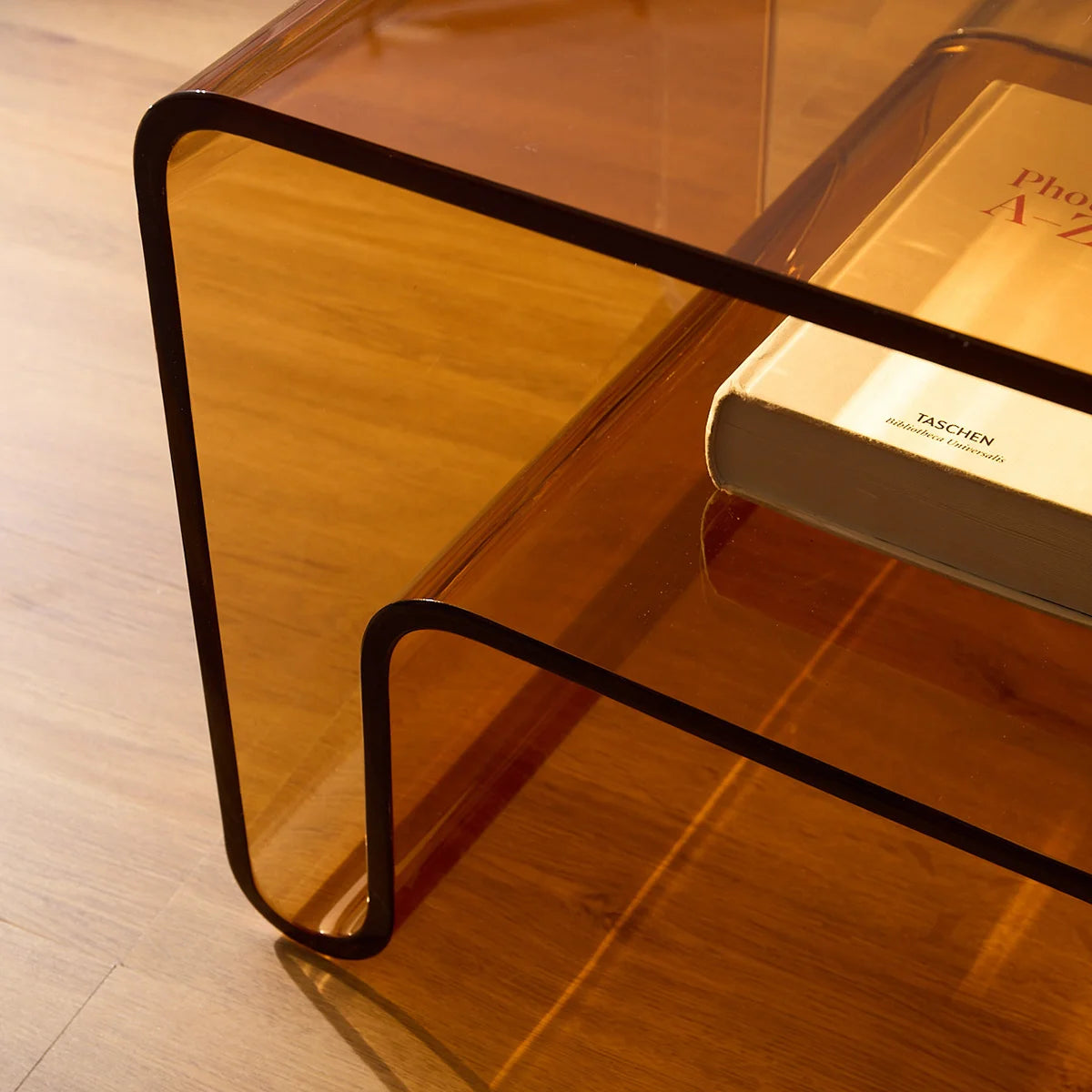 Mesa lateral Vértis em acrílico âmbar, vista de lado com livro.