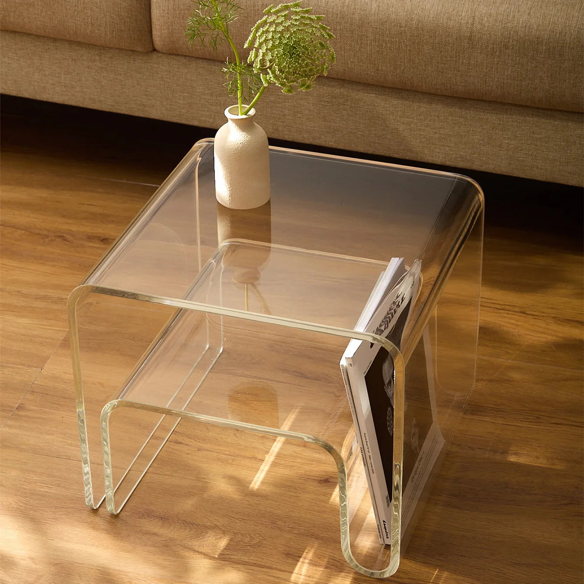 Mesa lateral Vértis em acrílico cristal, com vaso e revista ao lado do sofá.