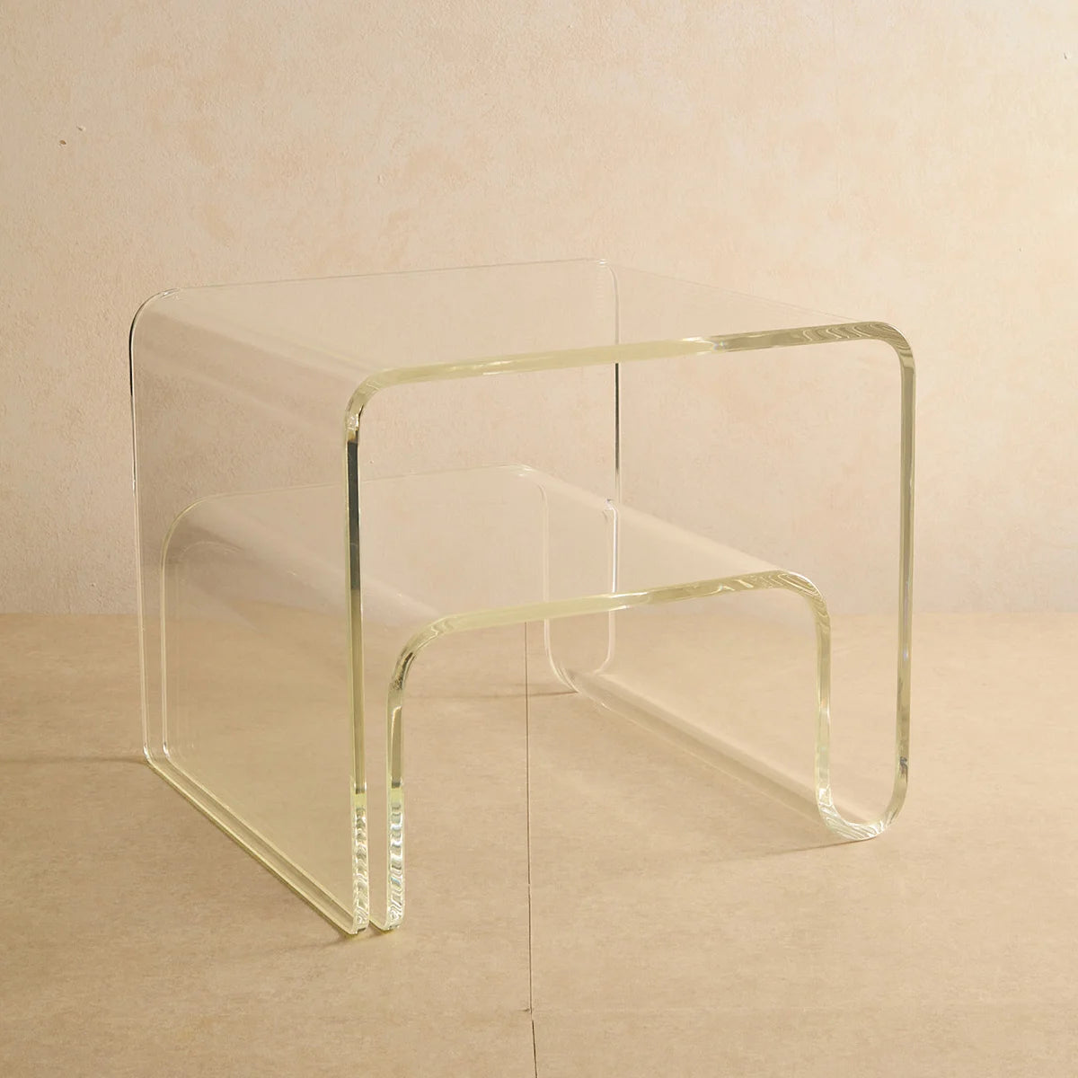 Mesa lateral Vértis em acrílico cristal, isolada sobre fundo bege.