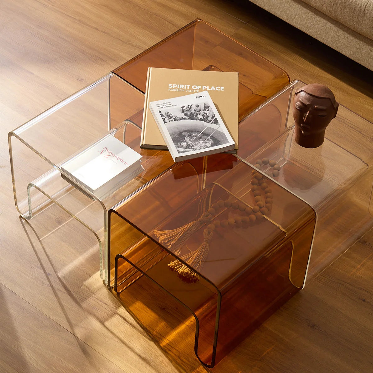 Mesa lateral Vértis em acrílico cristal, em composição com versão âmbar, livros e vaso.