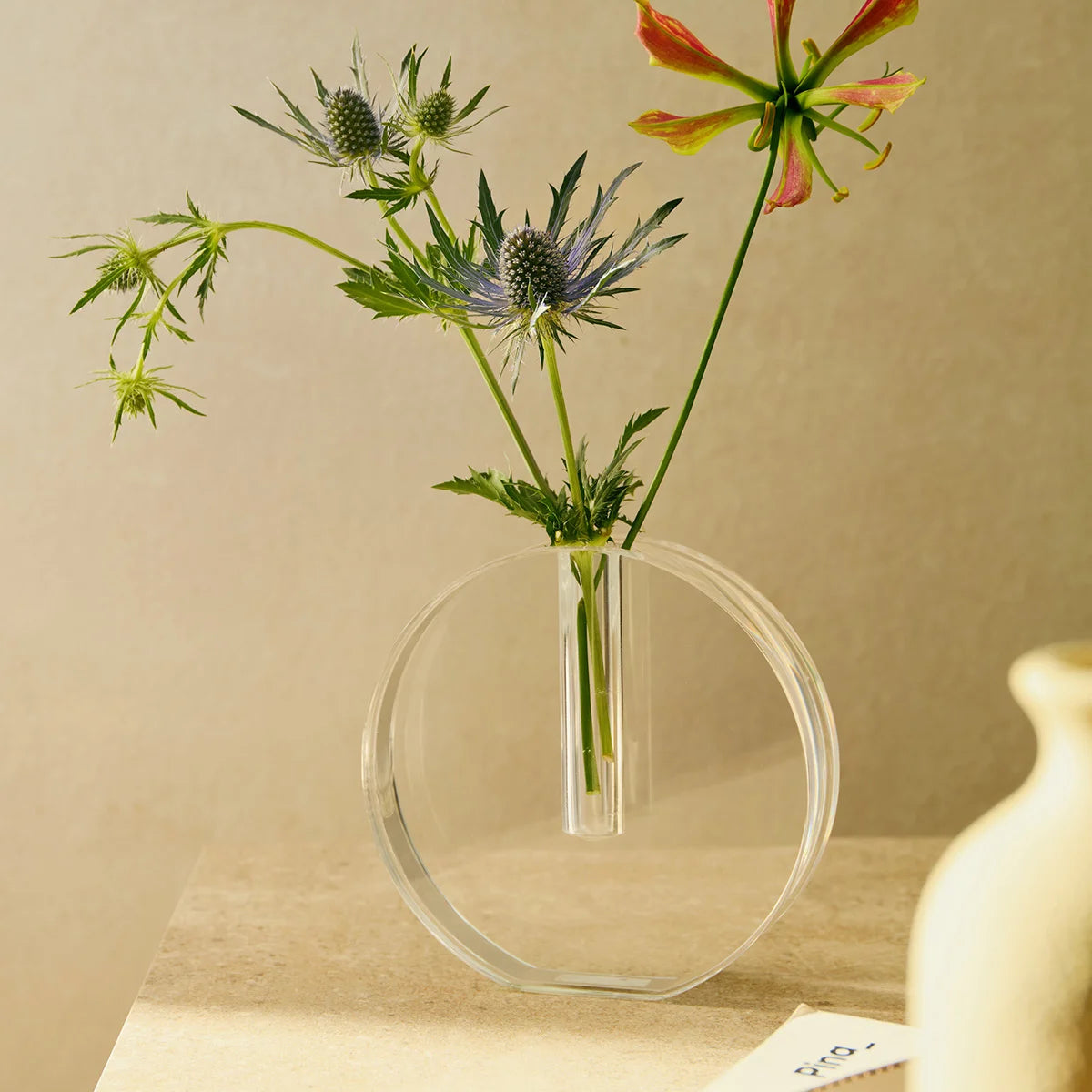 Vaso Sinué em acrílico cristal, com arranjo floral em ambiente iluminado.