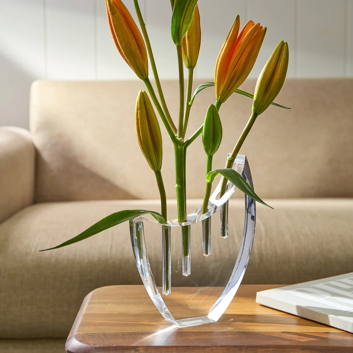 Vaso Selene em acrílico cristal, com flores em mesa ao lado do sofá.